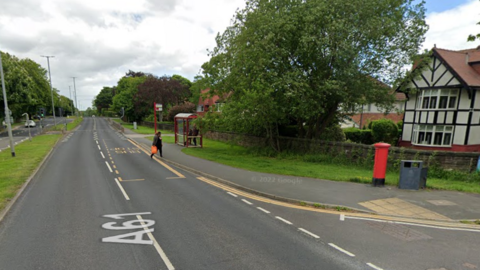 The A61 road in Leeds which shows a postbox, bus stop and large house on the corner of the junction.