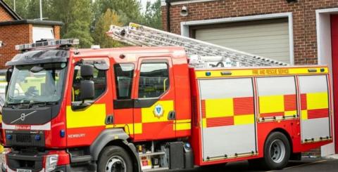 Fire engine parked outside a fire station garage - it is equipped with a large, extendable ladder.