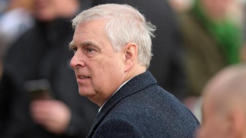 A profile shot of  Prince Andrew, Duke of York. He wears a dark herringbone blazer and has white hair.