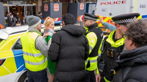 Green MP Hannah Spencer is by a police car surrounded by police officers and a man in a high vis jacket