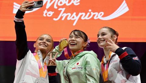 winners of womens floor gymnastics pose for selfie with medals on podium
