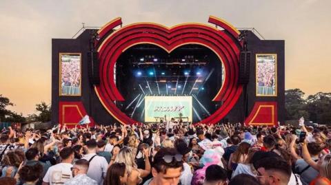 A stage at Love Saves The Day. The picture is taken from the back of the crowd, and the stage itself is black with a large red heart design around it. 