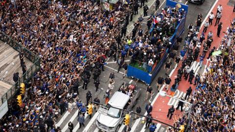 crowds of fans holding their arms out toward a passing float