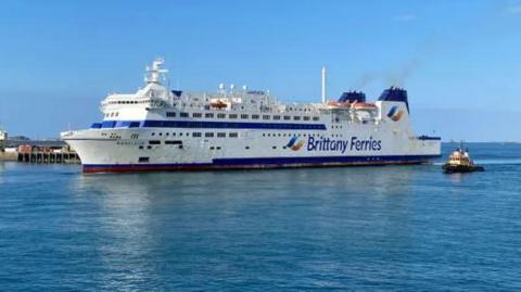 A white ferry with blue tipped chimneys with the words Brittany Ferries on the side arriving in St Peter Port Harbour.