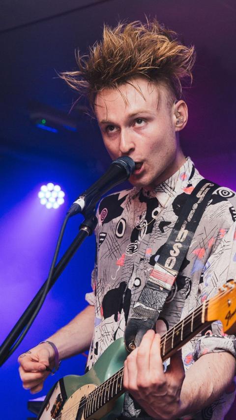 Look Mum No Computer, aka musician Sam Battle, on stage with guitar singing into a mic