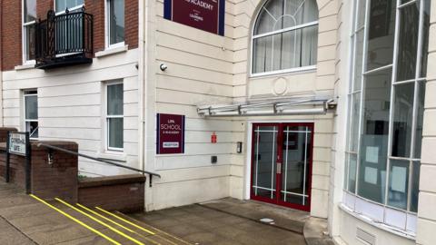 The doors to the school are closed. A sign says 'LIPA School 4-16 Academy reception'. A road sign outside the entrance says 'Cathedral Gate'.