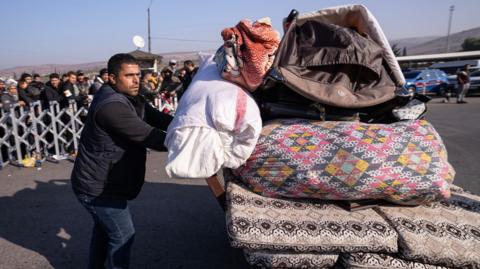 A man pushes a trolley carrying bedding. Behind him a queue of people wait to cross into Syria from Turkey at the Cilvegozu Border Gate on 9 December