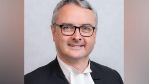Juan Watterson, who has short grey hair and is wearing glasses.