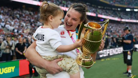 Abbie Ward celebrates winning the Women's Rugby World Cup last year as she holds the trophy and young daughter Hallie