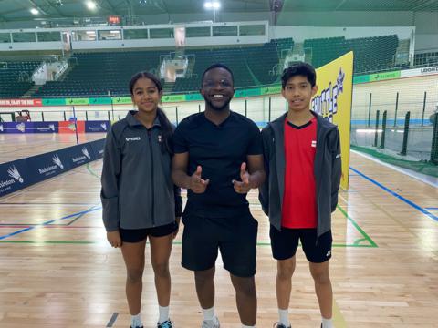 De Graft stands with two young Badminton players on the court.