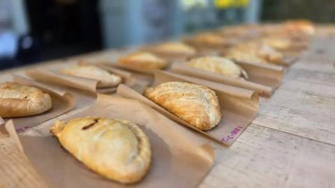 Several pasties lined up on paper bags on a wooden table.