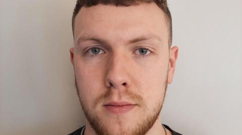 Custody picture of Benjamin Bottomley, a young man with a short beard. 