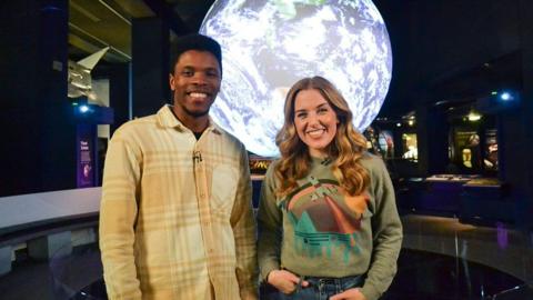 Presenters Rhys Stephenson and Maddie Moate in front of an image of the moon