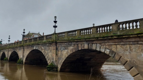 A bridge featuring four semi-circular arches above the river. At least three street lamps are on the bridge, which goes from left to right on the photo.