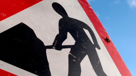 A large red, white and black sign with an image of a man with a shovel on it