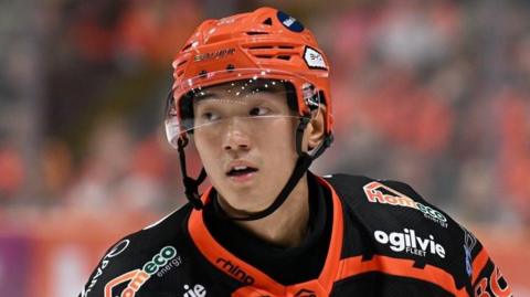 Cliff Pu wearing a black and orange ice hockey top and an orange helmet with a transparent visor.
