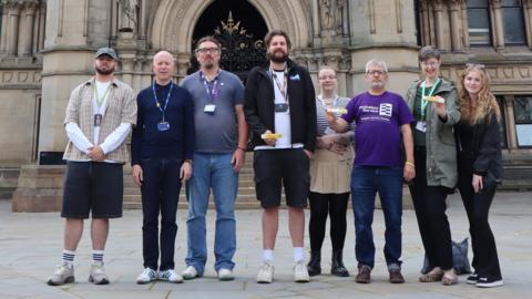 A line up of men and women with some holding a small yellow box which contains the Naloxone syringe 