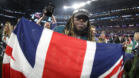 Jay Ajayi holds the UK flag at the Superbowl