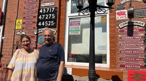 Eric and Wendy Coupe standing in the sunshine outside their red brick terraced house covered in vintage railway signs