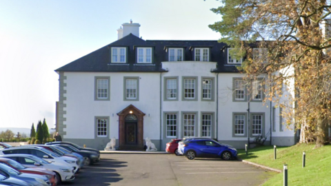 A hotel building with cars parked outside and trees on the lawns in front of it