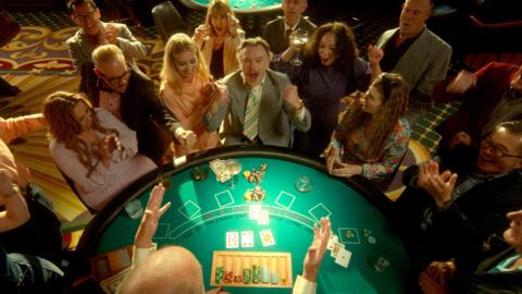 a crowd gathers around a poker table. One man is cheering in victory as the group around him claps — Seems he's won a big match