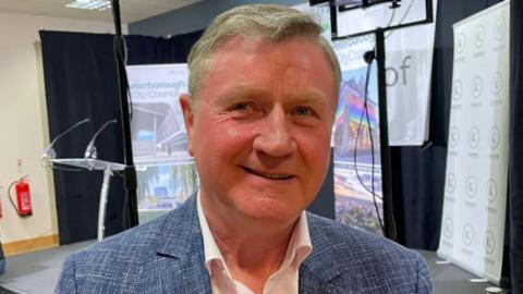 Dennis Jones wearing a blue blazer and a white shirt, smiling for the camera.