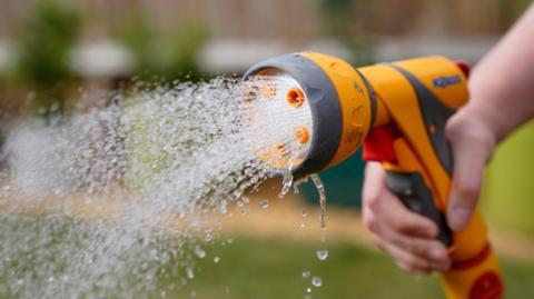 A person holds a hosepipe with water gushing out of it