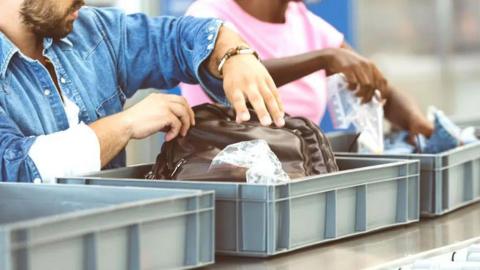 Two people sorting their luggage into grey airport trays