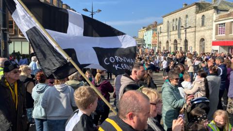 A crowd of people celebrating St Piran's Day - with a black and white flag prominent