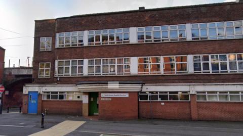 A red brick building. It has many windows. A blue door to the left. And it is a cloudy day.