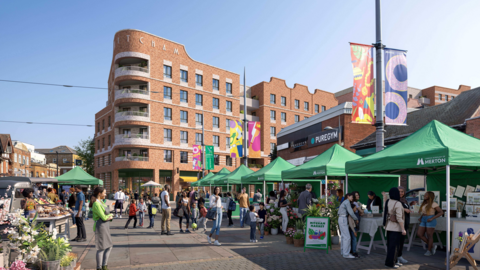 A computer-generated image shows a large brick building with a curved front standing above a market with green canopies and various stallholders and shoppers. 
