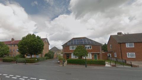 Houses line a road with low hedges and road in front narrow road to close with further homes behind