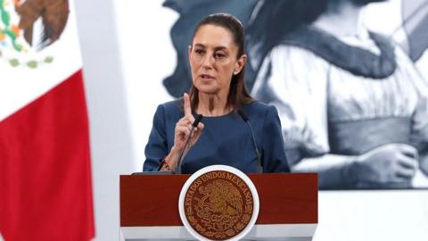Mexican PM Claudia Sheinbaum speaks behind a podium. 