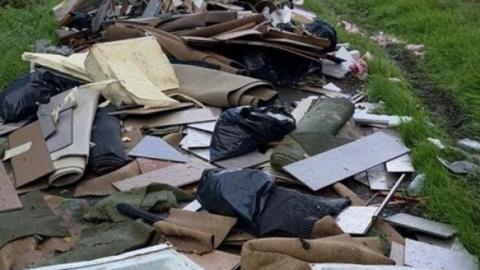 A fly-tip of rubbish strewn along a field