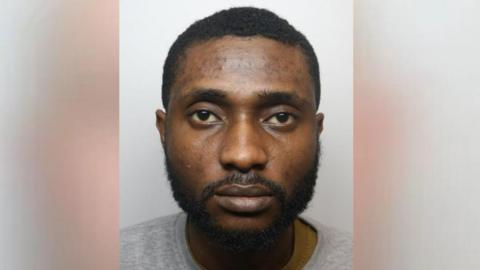 Mugshot of Chiemka Okoronta. He is wearing as grey sweatshirt and has short black hair and a beard. 