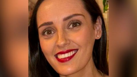 Jodie Mitchell - woman with long dark hair, looking into the camera smiling, wearing red lipstick and small diamond stud earrings