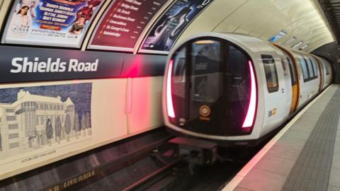 A white and orange subway train pulling away from Shields Road station.