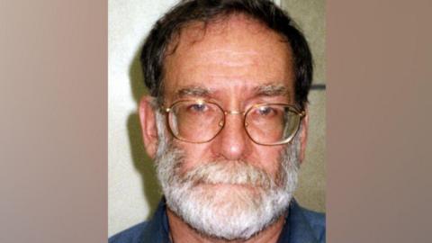 Police custody image of GP Harold Shipman with dark grey hair, light grey beard and glasses