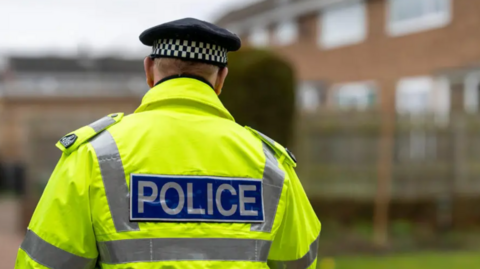 A stock image of a police officer in a high-viz police jacket. The officer's back is to the camera.