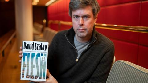 David Szalay holding up the cover of his novel Flesh