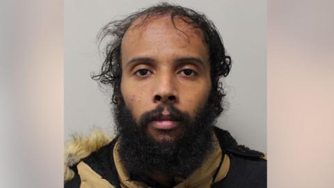 Close-up custody-style photograph of Waleed Saeed, facing the camera against a plain background. He has thin dark hair on top, longer hair at the sides, and a full beard. He is wearing a dark jacket with a light-coloured, fur-trimmed hood.