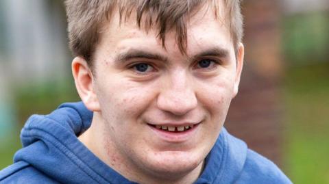 Owen Garnett, in a blue hooded top, smiles at the camera, looking happy.