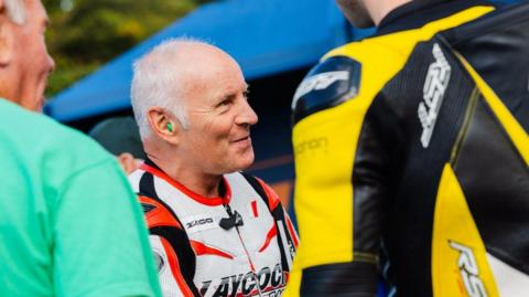 Ian Lougher, who has grey hair and is wearing white, red and black leathers, in the paddock at a race.