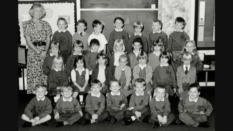 A black and white school photo showing smiling pupils and their teacher.