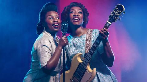 Artwork from the show Marie and Rosetta. The photo pictures two women dressed in 1940s dresses. The woman on the left is holding a microphone and singing joyfully. The woman on the right, Beverley Knight is smiling and holding a guitar.