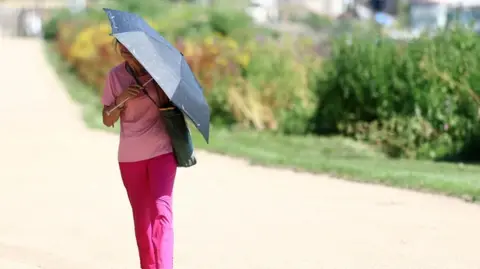 A person uses an umbrella to shield from the sun whilst walking along the River Thames, as Britain experiences record temperatures disrupting schools and transport networks, at Richmond, in London, Britain, June 25, 2026
