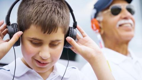 A boy wearing headphones smiles while looking down.