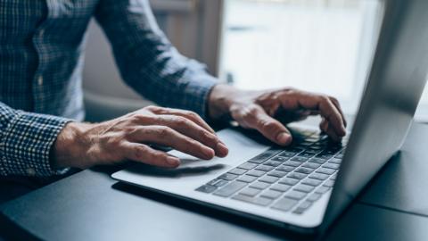 Stock photo shows a close up of a person's hands typing on computer keyboard at home