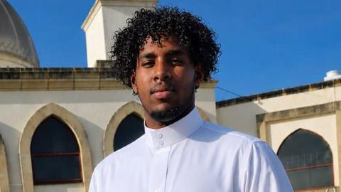 A man wearing white with curly dark hair and facial hair.