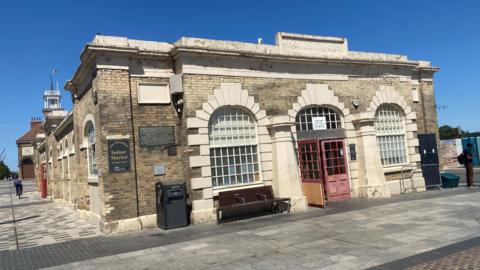 An outside view of the Stockton Shambles building. It has open red doors in the centre of stone archways with windows. 